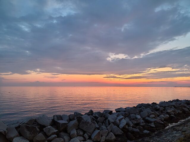 Abendrot über dem Meer bei Grado, im Vordergrund Steine einer Mole