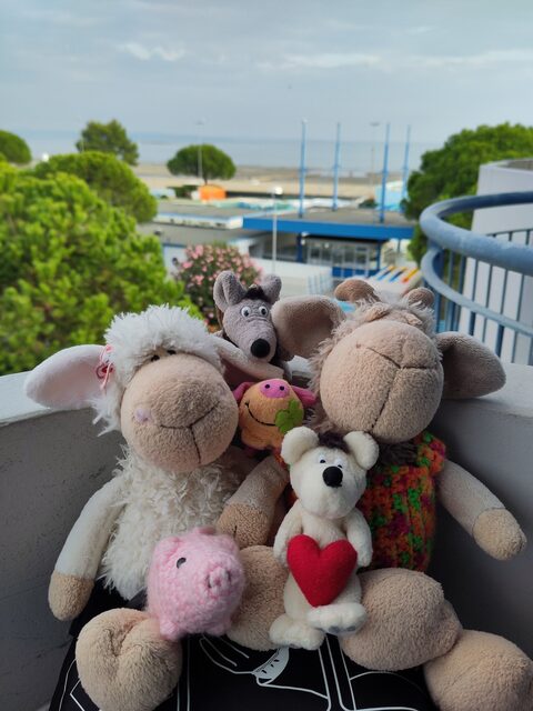 Eine Gruppe Kuscheltiere auf einem Balkon, im Hintergrund das Meer