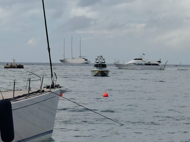 Blick vom Hafen aufs Meer, im Hintergrund die weiße Sailing Yacht A mit ihren drei hohen Masten, davor kleinere Boote