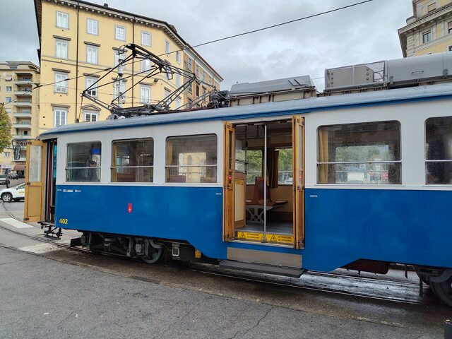 Seitenansicht des blau-weißen Opicina-Triebwagens 402 mit offener Holztür und Holzbänken im Inneren